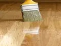 Pennello applica vernice lucida su parquet. La tabella gloss vernici mostra la brillantezza ottenuta.