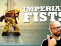 Miniatura di un guerriero degli Imperial Fists, giallo e rosso, con fucile. Un uomo con occhiali fa pollice in su.