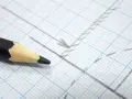 Matita nera su carta millimetrata con linee e frecce disegnate, utile per calcolare la proporzione per trovare la scala di un disegno.