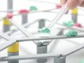 Pinzette posizionano un'auto verde su una **tokyo highway** in miniatura, con altre auto rosse e verdi sparse sulla struttura.