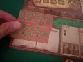 Dettaglio del gioco da tavolo "Marco Polo". Una mano posiziona una tessera con numeri verdi su una plancia di gioco in legno.