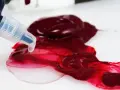 Un beccuccio trasparente rilascia un liquido chiaro su un colore acrilico rosso intenso, mostrando come diluire i colori acrilici per ottenere sfumature più leggere.