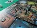 Miniature di eroi si preparano ad affrontare le oscure trame di un gioco da tavolo, tra barili e rune luminose, in un'avventura ricca di tales of evil.