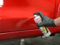 Mano con guanto nero spruzza prodotto su vernice rossa lucida, per rimuovere residui e capire come rendere opaca una vernice lucida.