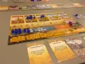 Un gioco da tavolo che ripercorre le ere, con pedine blu e gialle che rappresentano risorse e unità, carte evento e un tabellone di civiltà.