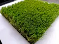 Un campione di erba sintetica, verde brillante e folta, mostra come fare l'erba finta per un giardino perfetto.
