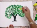 Mano che dipinge alberi con cotton fioc, creando un effetto di fogliame con tanti piccoli cerchi verdi.