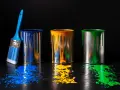 Tre barattoli di vernice blu, gialla e verde gocciolano su un tavolo di legno scuro. Un pennello blu è appoggiato al barattolo blu. Un'alternativa all'alcool isopropilico per pulire?