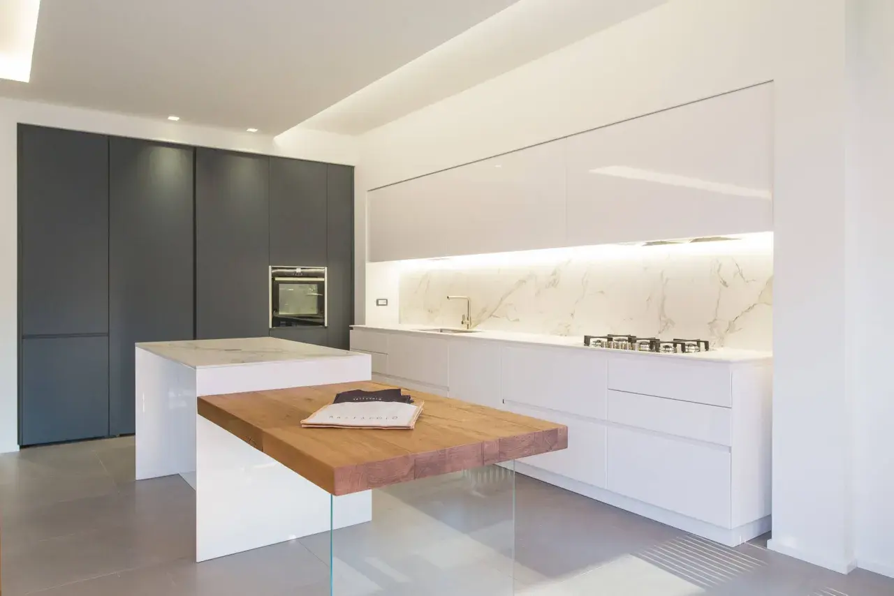 Cucina moderna con isola centrale in legno e marmo. Mobili bianchi lucidi e un piano in marmo creano eleganti sfumature di bianco, contrastando con le ante scure.