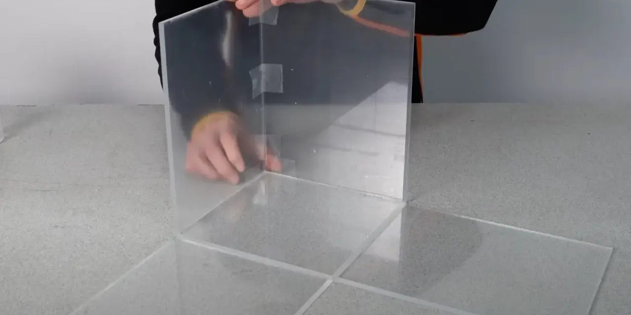 Costruzione di una teca in plexiglass fai da te, con pannelli trasparenti assemblati con nastro adesivo.