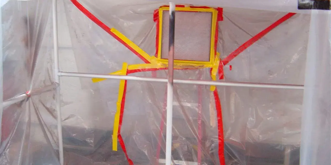 Struttura fai da te per verniciatura, con teli trasparenti e nastro giallo/rosso a delimitare l'area.