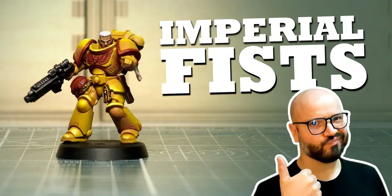 Miniatura di un guerriero degli Imperial Fists, giallo e rosso, con fucile. Un uomo con occhiali fa pollice in su.
