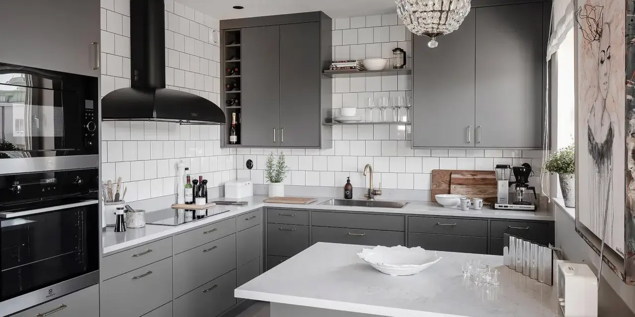 Cucina moderna con mobili color titanio, cappa nera, piano in quarzo bianco e lampadario di cristallo.
