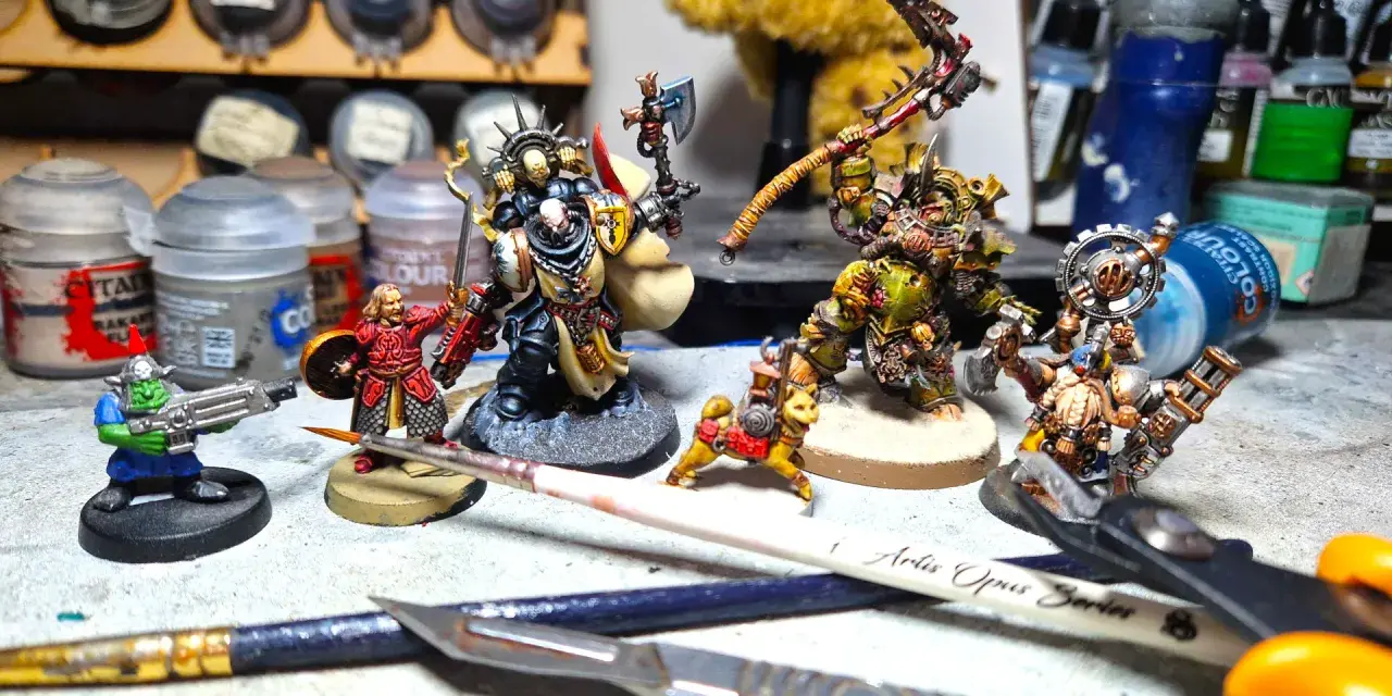 Miniature di Death Korps of Krieg e altri guerrieri pronti per la battaglia, circondati da colori e attrezzi per modellismo.