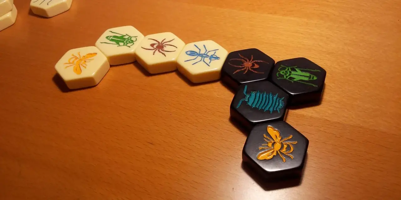 Pezzi esagonali del **hive gioco da tavolo** con insetti colorati disposti su un tavolo di legno.