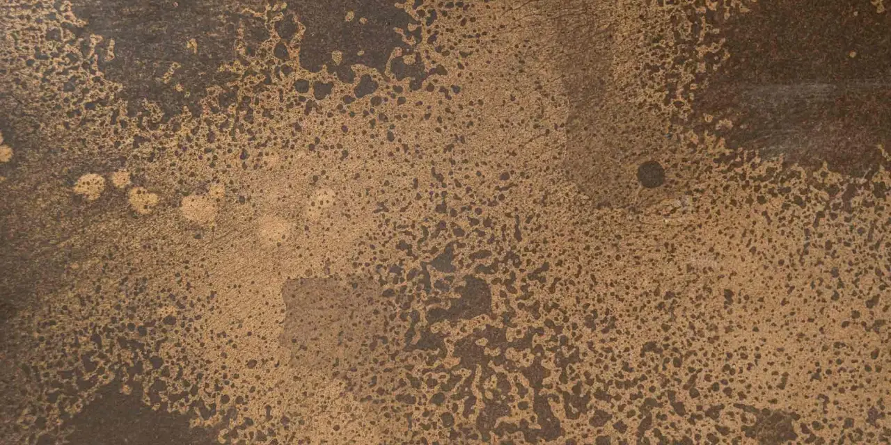 Superficie ruvida con macchie scure su sfondo dorato, che colore è il bronzo.
