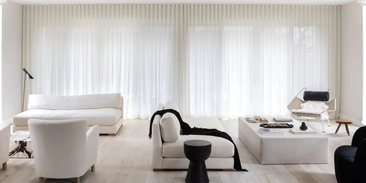 Soggiorno minimalista con divani bianchi, poltrone soffici e tende leggere. Un tocco di nero spezza la palette, creando 50 sfumature di bianco e contrasto.