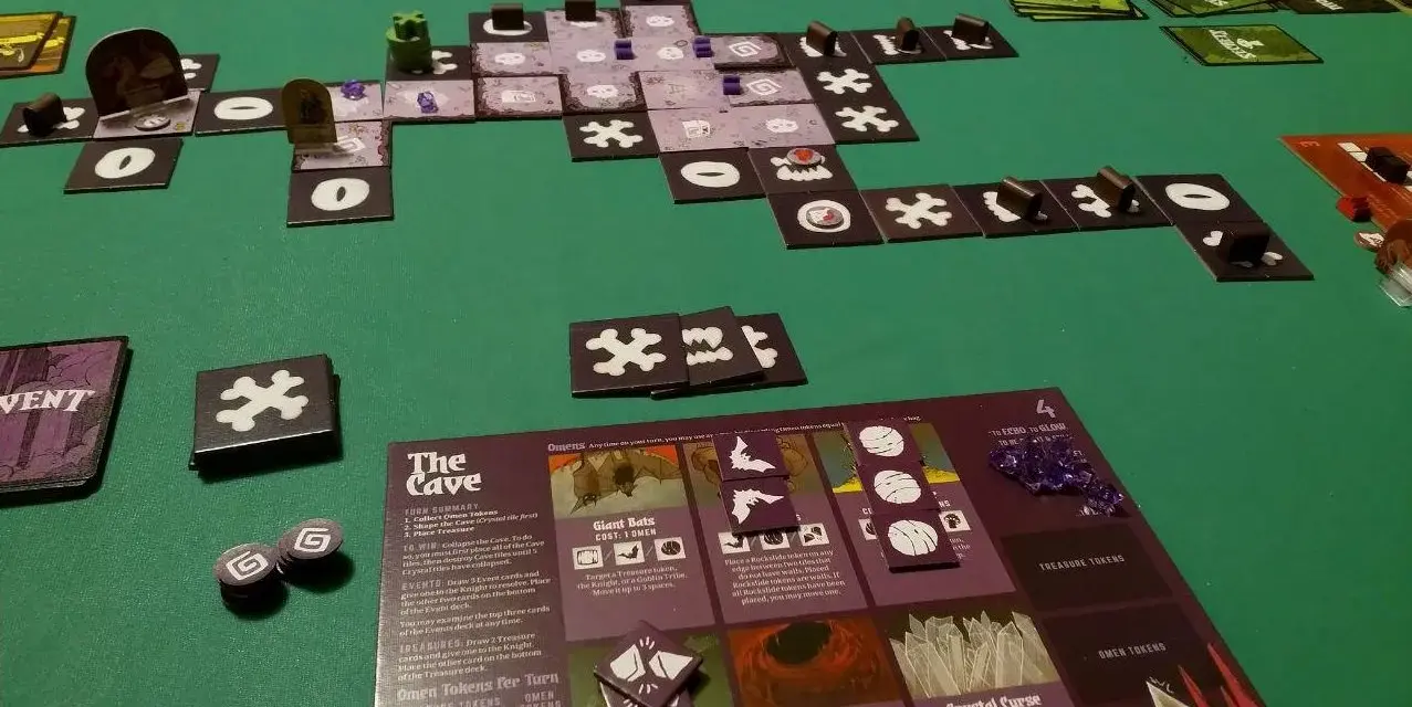 Vasto gioco da tavolo "The Cave" con tessere, carte e segnalini su un tappetino verde.