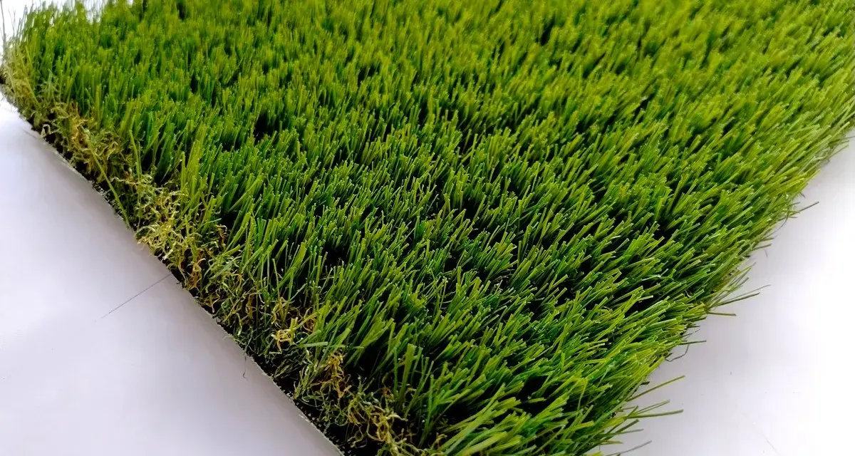 Un campione di erba sintetica, verde brillante e folta, mostra come fare l'erba finta per un giardino perfetto.