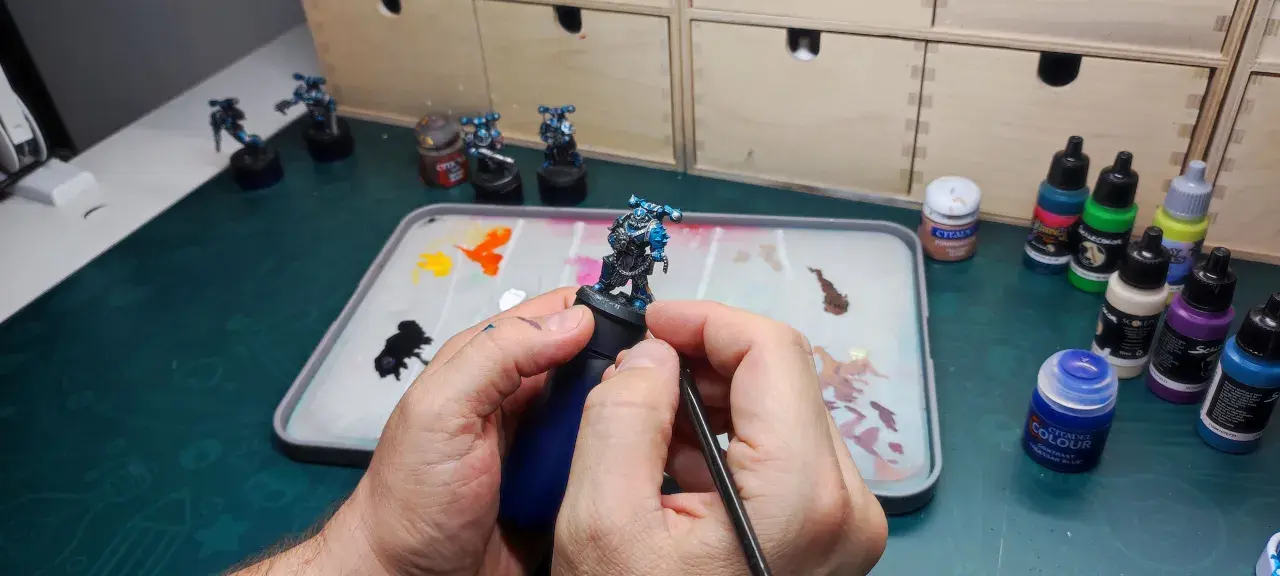 Mani che dipingono miniature, con pennello e tavolozza piena di colori.