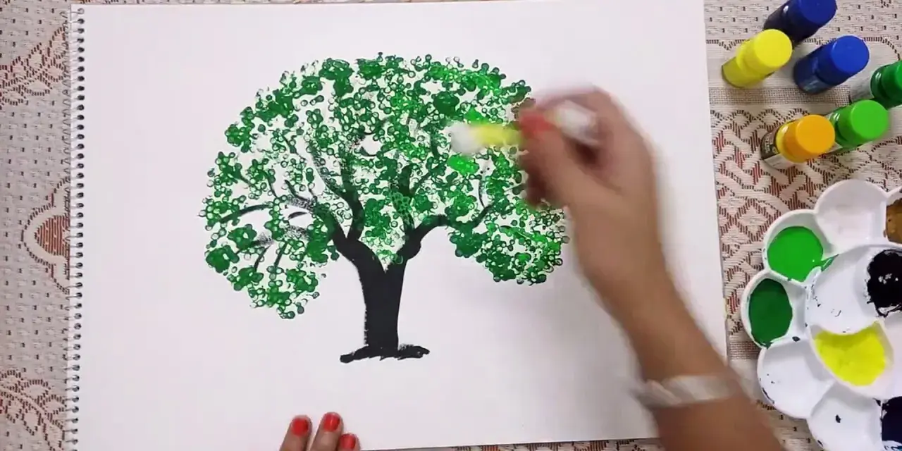 Mano che dipinge alberi con cotton fioc, creando un effetto di fogliame con tanti piccoli cerchi verdi.