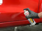 Mano con guanto nero spruzza prodotto su vernice rossa lucida, per rimuovere residui e capire come rendere opaca una vernice lucida.