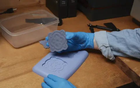 Mani guantate che estraggono un motivo floreale da stampi fai da te in silicone.