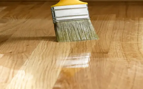 Pennello applica vernice lucida su parquet. La tabella gloss vernici mostra la brillantezza ottenuta.