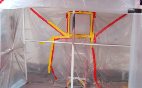 Struttura fai da te per verniciatura, con teli trasparenti e nastro giallo/rosso a delimitare l'area.