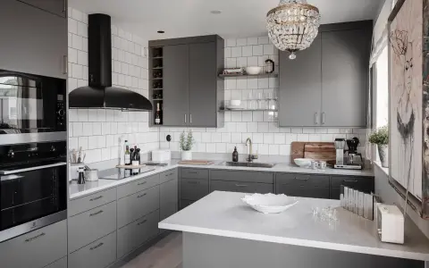 Cucina moderna con mobili color titanio, cappa nera, piano in quarzo bianco e lampadario di cristallo.