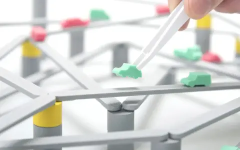 Pinzette posizionano un'auto verde su una **tokyo highway** in miniatura, con altre auto rosse e verdi sparse sulla struttura.