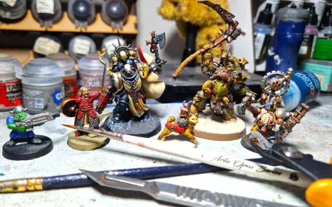 Miniature di Death Korps of Krieg e altri guerrieri pronti per la battaglia, circondati da colori e attrezzi per modellismo.