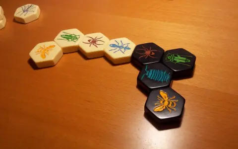 Pezzi esagonali del **hive gioco da tavolo** con insetti colorati disposti su un tavolo di legno.