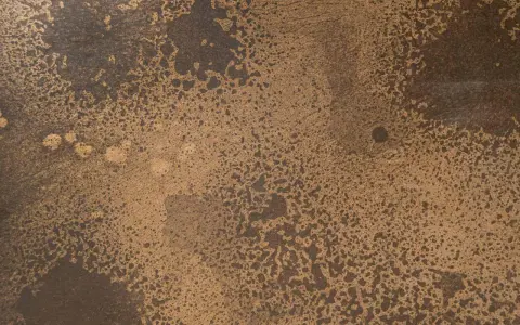 Superficie ruvida con macchie scure su sfondo dorato, che colore è il bronzo.