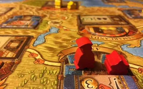 Pedine rosse su un tabellone di giochi da tavolo gestionali, con dadi e città sullo sfondo.