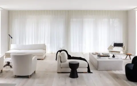 Soggiorno minimalista con divani bianchi, poltrone soffici e tende leggere. Un tocco di nero spezza la palette, creando 50 sfumature di bianco e contrasto.