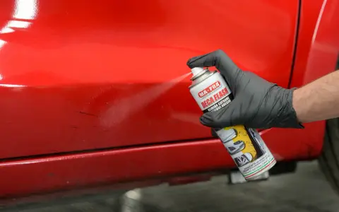 Mano con guanto nero spruzza prodotto su vernice rossa lucida, per rimuovere residui e capire come rendere opaca una vernice lucida.