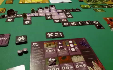 Vasto gioco da tavolo "The Cave" con tessere, carte e segnalini su un tappetino verde.