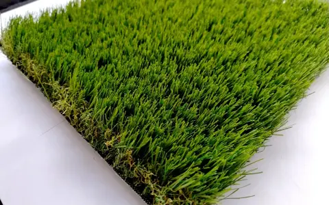 Un campione di erba sintetica, verde brillante e folta, mostra come fare l'erba finta per un giardino perfetto.