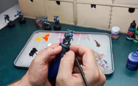 Mani che dipingono miniature, con pennello e tavolozza piena di colori.