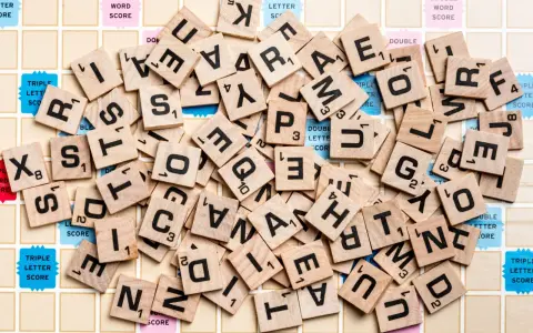 Un mucchio di tessere di Scarabeo sparse sul tabellone. Quante lettere si danno a Scarabeo per formare parole?