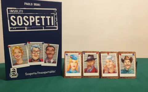 Il gioco "Insoliti Sospetti" presenta una scatola blu con ritratti di personaggi e carte con volti di sospetti, pronti per essere identificati.