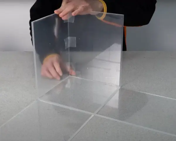 Costruzione di una teca in plexiglass fai da te, con pannelli trasparenti assemblati con nastro adesivo.