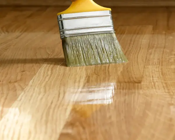 Pennello applica vernice lucida su parquet. La tabella gloss vernici mostra la brillantezza ottenuta.