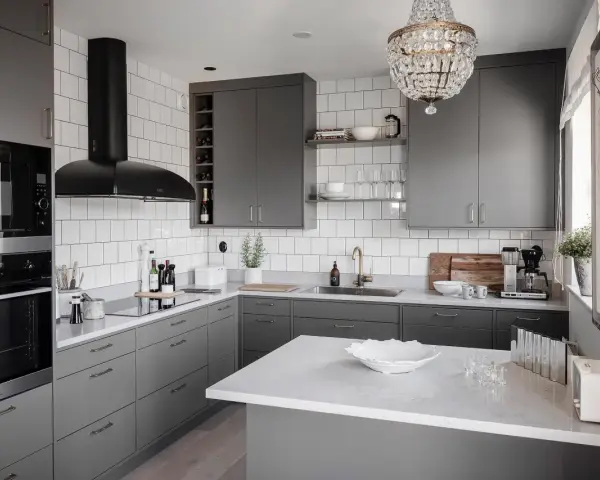 Cucina moderna con mobili color titanio, cappa nera, piano in quarzo bianco e lampadario di cristallo.