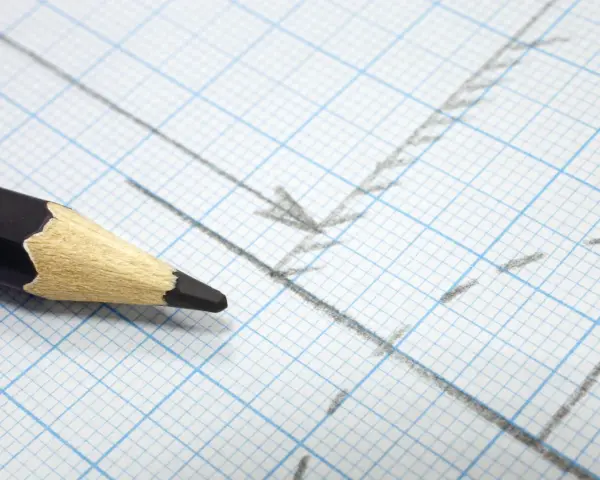 Matita nera su carta millimetrata con linee e frecce disegnate, utile per calcolare la proporzione per trovare la scala di un disegno.