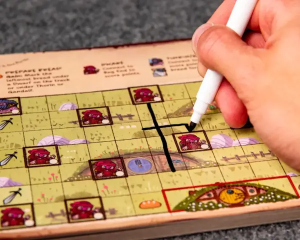 Mano che segna una casella su una plancia colorata, parte del gioco da tavolo "Hobbit il gioco".
