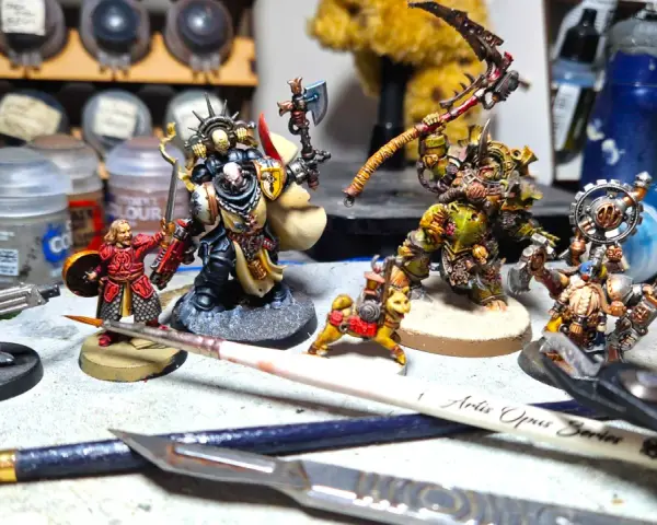 Miniature di Death Korps of Krieg e altri guerrieri pronti per la battaglia, circondati da colori e attrezzi per modellismo.