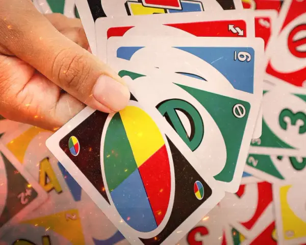 Mano che tiene carte UNO, pronte per una partita di "20 domande". Numeri, colori e simboli si mescolano in un gioco di strategia.