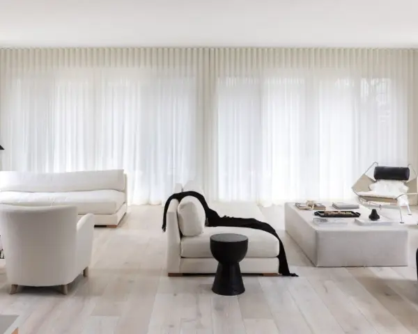 Soggiorno minimalista con divani bianchi, poltrone soffici e tende leggere. Un tocco di nero spezza la palette, creando 50 sfumature di bianco e contrasto.